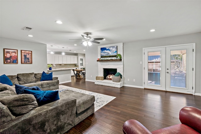 living room with french doors, a brick fireplace, ceiling fan, dark wood-type flooring, and brick wall