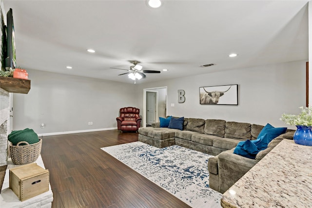 living room featuring ceiling fan, a stone fireplace, and dark hardwood / wood-style flooring