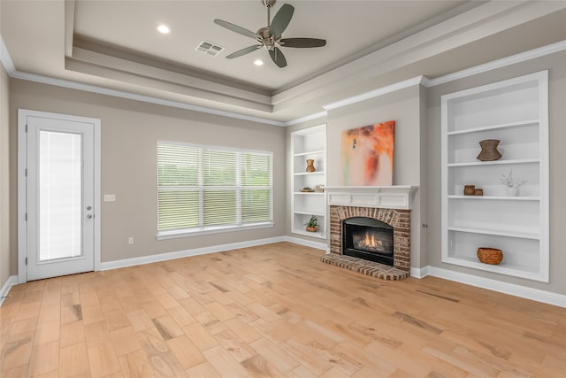 unfurnished living room featuring a brick fireplace, a raised ceiling, ceiling fan, ornamental molding, and light hardwood / wood-style flooring