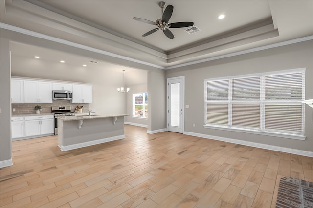 kitchen featuring stainless steel appliances, an island with sink, a kitchen breakfast bar, a tray ceiling, and white cabinetry