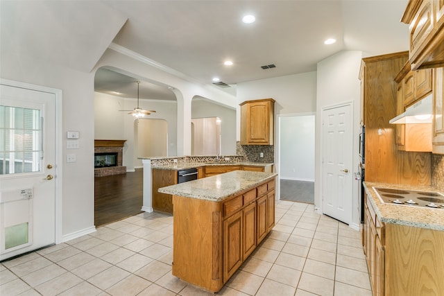 kitchen featuring white electric stovetop, light tile patterned floors, a brick fireplace, backsplash, and kitchen peninsula