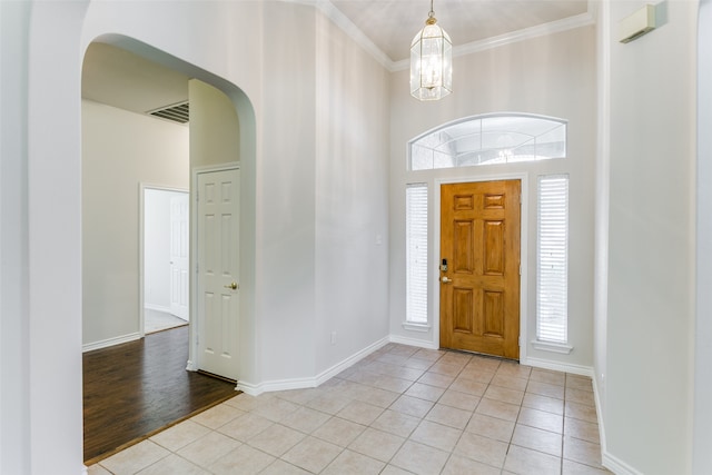 entryway featuring ornamental molding, tile patterned floors, an inviting chandelier, and a high ceiling