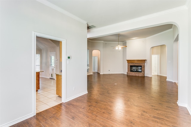 unfurnished living room featuring ceiling fan, tile patterned floors, a fireplace, and crown molding