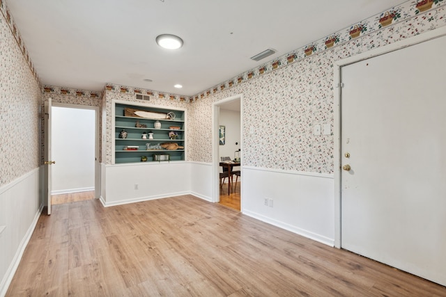 spare room featuring built in shelves and light wood-type flooring