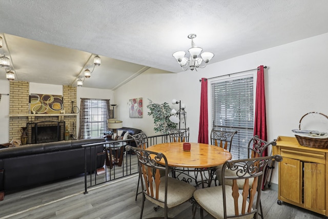 dining room with wood-type flooring, lofted ceiling, a fireplace, and a chandelier