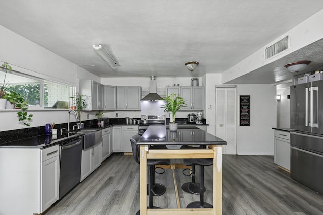 kitchen with hardwood / wood-style floors, wall chimney exhaust hood, gray cabinets, a textured ceiling, and appliances with stainless steel finishes