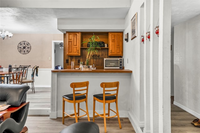 kitchen with a kitchen breakfast bar, kitchen peninsula, light hardwood / wood-style floors, and an inviting chandelier