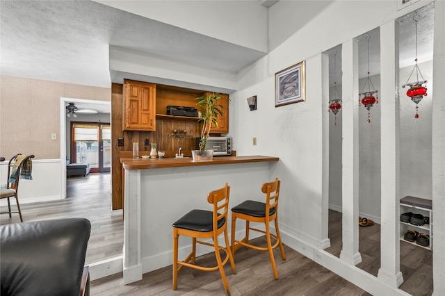 kitchen with kitchen peninsula, light wood-type flooring, ceiling fan, and a breakfast bar area