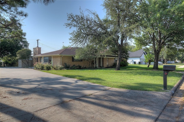 view of front of property featuring driveway, brick siding, a chimney, and a front yard