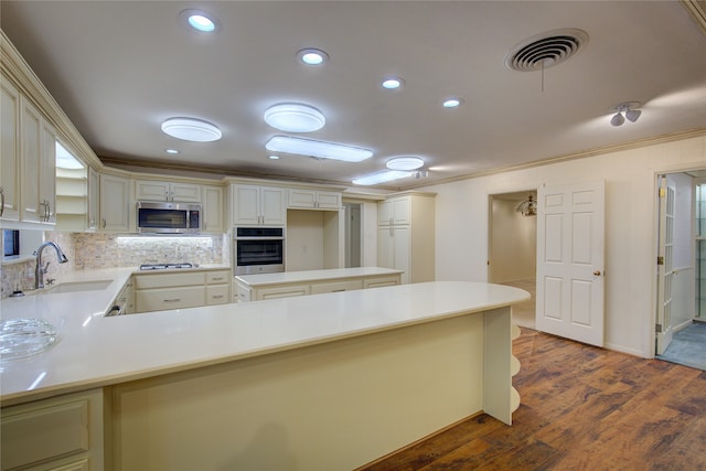 kitchen with stainless steel appliances, hardwood / wood-style floors, sink, ornamental molding, and kitchen peninsula