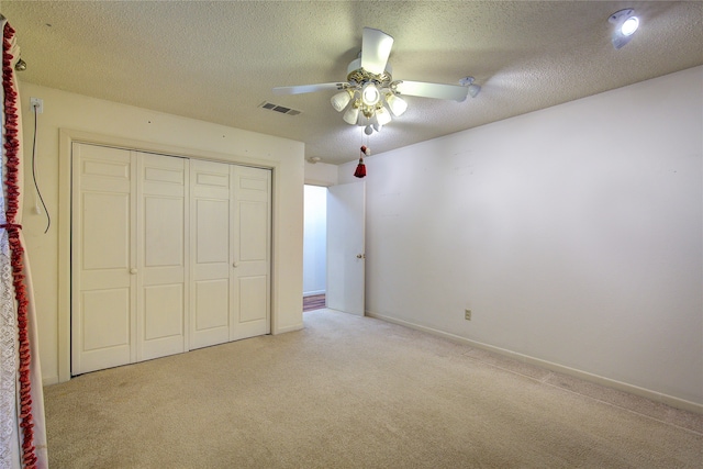 unfurnished bedroom featuring ceiling fan, a closet, a textured ceiling, and light colored carpet