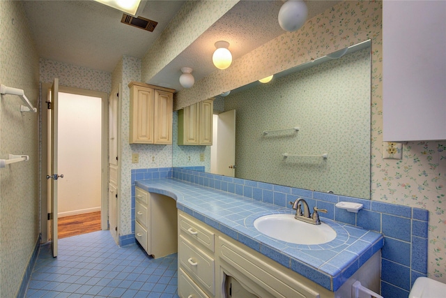 bathroom with visible vents, vanity, tile patterned flooring, baseboards, and wallpapered walls