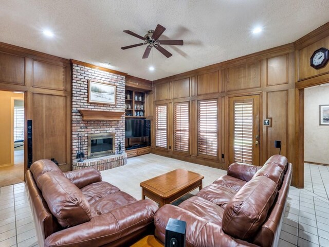 carpeted living room featuring a textured ceiling, ceiling fan, a brick fireplace, wood walls, and built in features