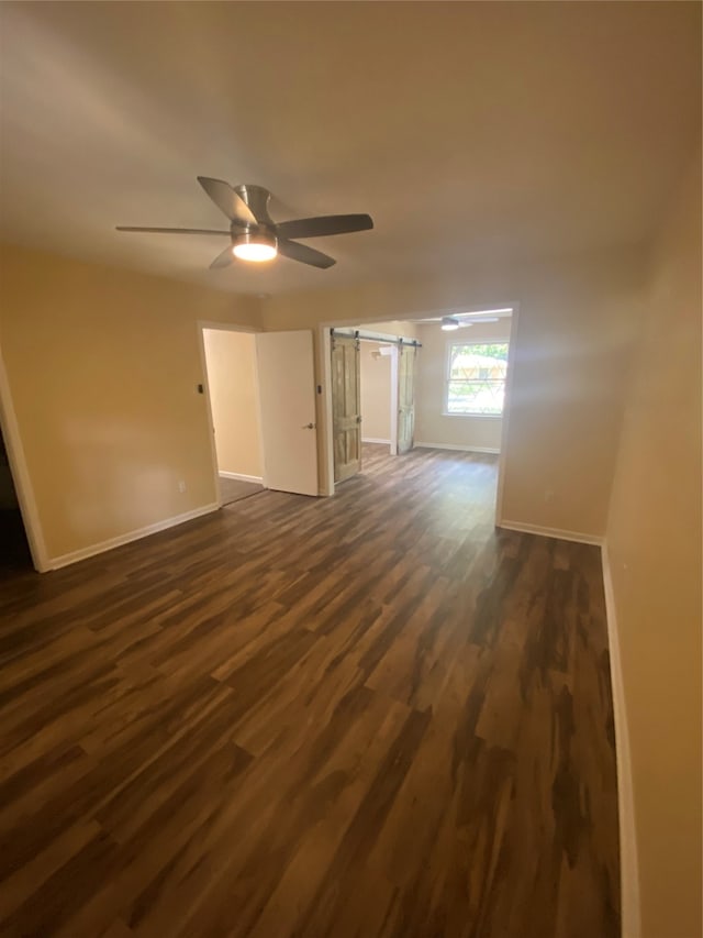 spare room featuring a barn door, dark hardwood / wood-style floors, and ceiling fan