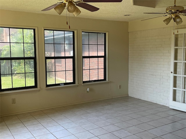 tiled spare room featuring a textured ceiling, brick wall, and ceiling fan