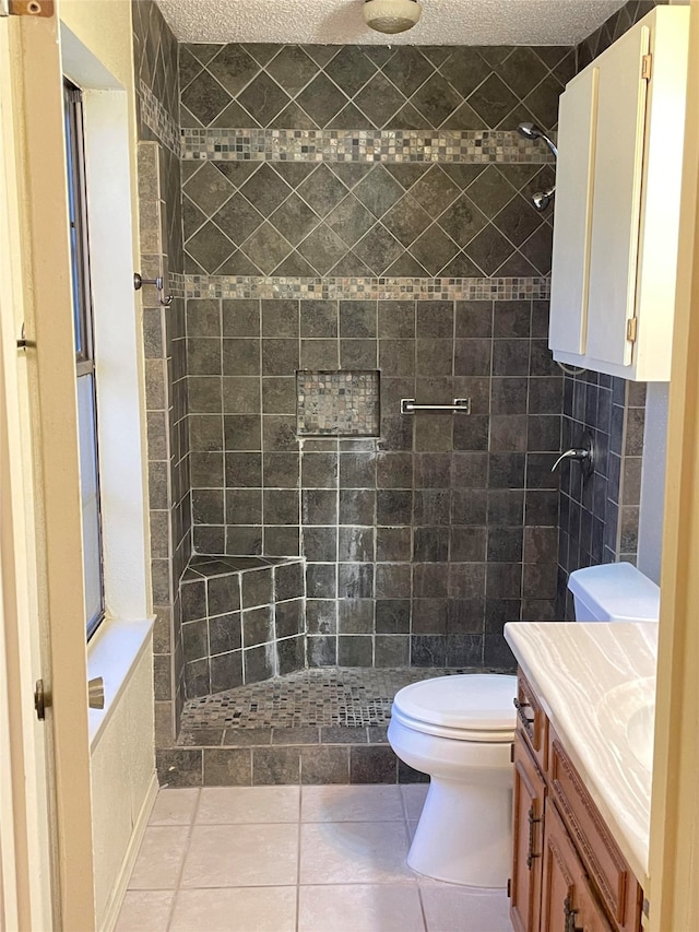 bathroom with vanity, tile patterned flooring, a textured ceiling, a tile shower, and toilet