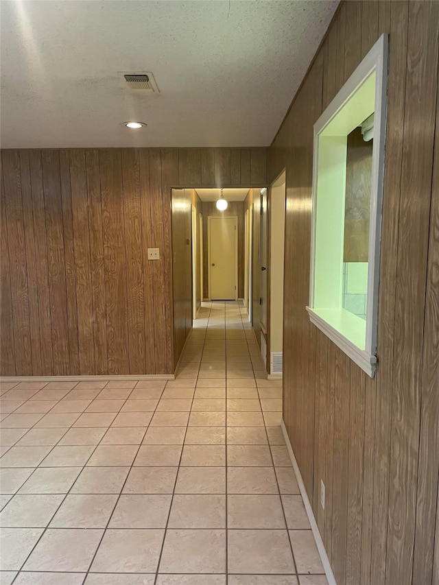 hallway with wood walls, a textured ceiling, and light tile patterned floors