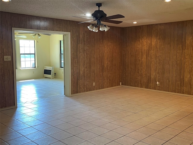 tiled empty room featuring ceiling fan, a textured ceiling, and wooden walls