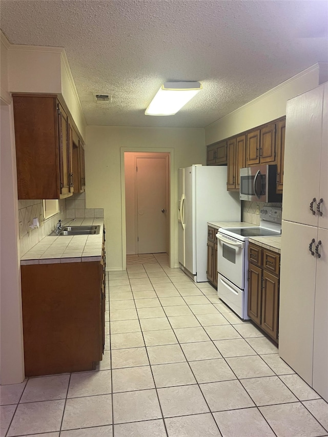 kitchen with light tile patterned floors, backsplash, sink, and white appliances