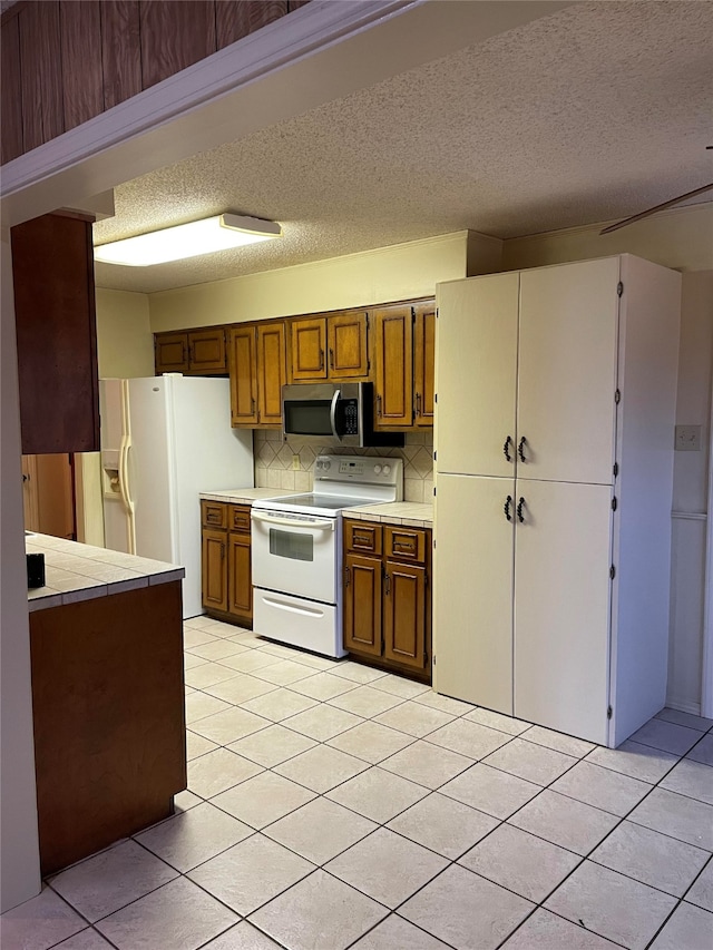 kitchen with tasteful backsplash, a textured ceiling, tile countertops, white appliances, and light tile patterned flooring