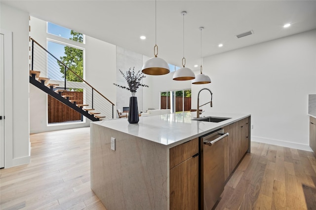 kitchen featuring an island with sink, light hardwood / wood-style floors, sink, and hanging light fixtures