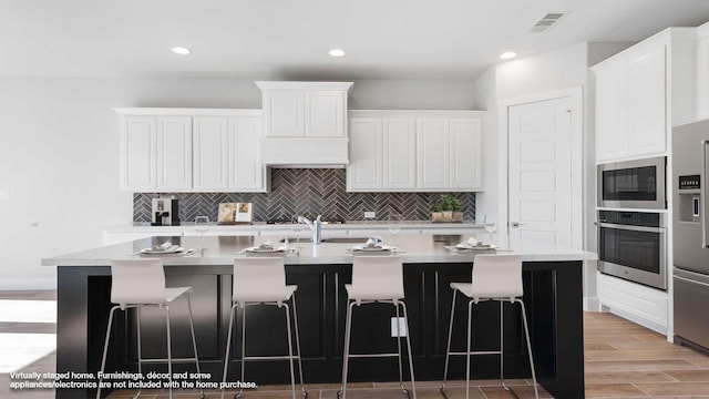 kitchen with a kitchen breakfast bar, a center island with sink, appliances with stainless steel finishes, white cabinets, and tasteful backsplash