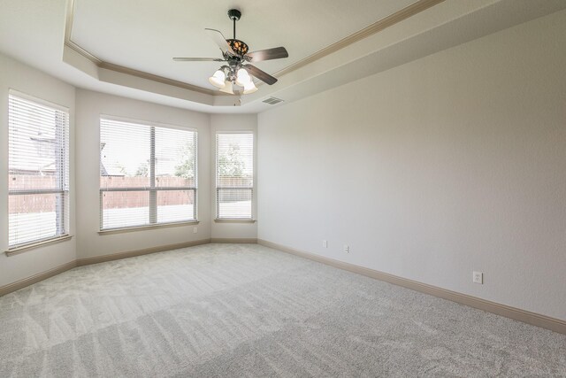 carpeted spare room with crown molding, a tray ceiling, ceiling fan, and plenty of natural light