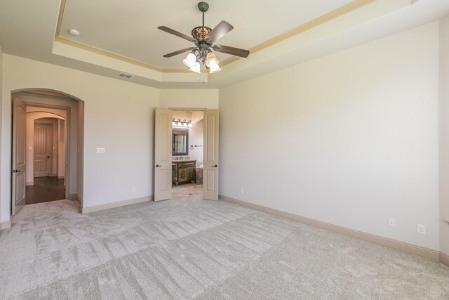 unfurnished bedroom with ceiling fan, a raised ceiling, ensuite bath, and light carpet