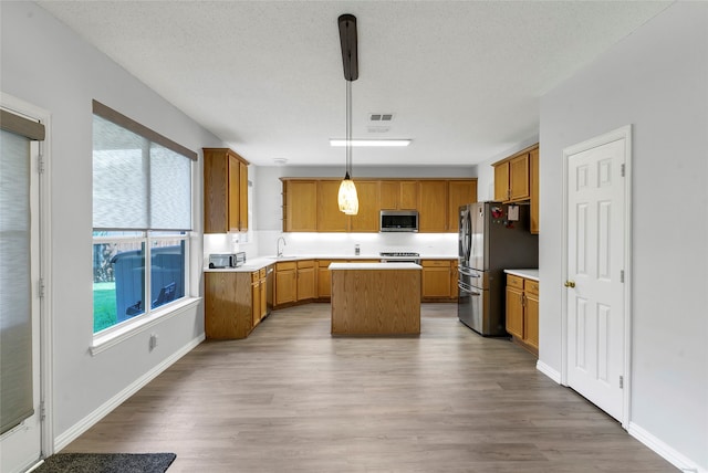 kitchen with appliances with stainless steel finishes, sink, pendant lighting, a kitchen island, and wood-type flooring