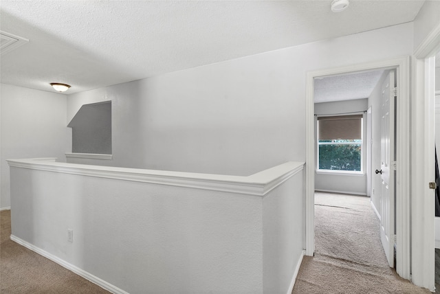 hallway with light carpet and a textured ceiling