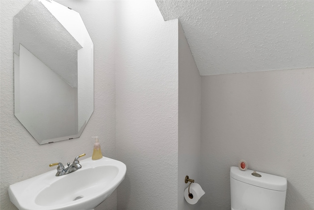 bathroom featuring sink, a textured ceiling, vaulted ceiling, and toilet