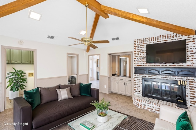 carpeted living room featuring a brick fireplace, lofted ceiling with beams, and ceiling fan