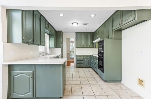 kitchen with green cabinetry, light tile patterned floors, black oven, and kitchen peninsula