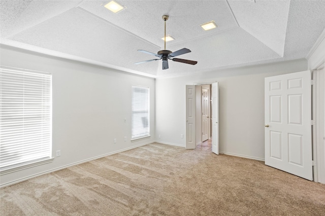 unfurnished bedroom featuring ceiling fan, light carpet, a textured ceiling, and a tray ceiling