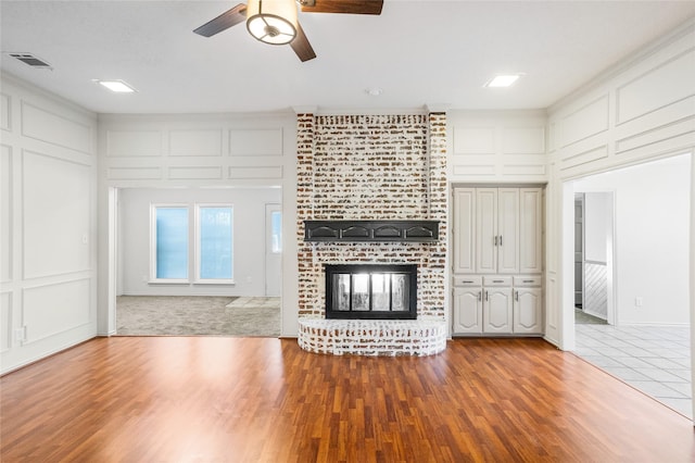 unfurnished living room featuring a brick fireplace, hardwood / wood-style flooring, and ceiling fan