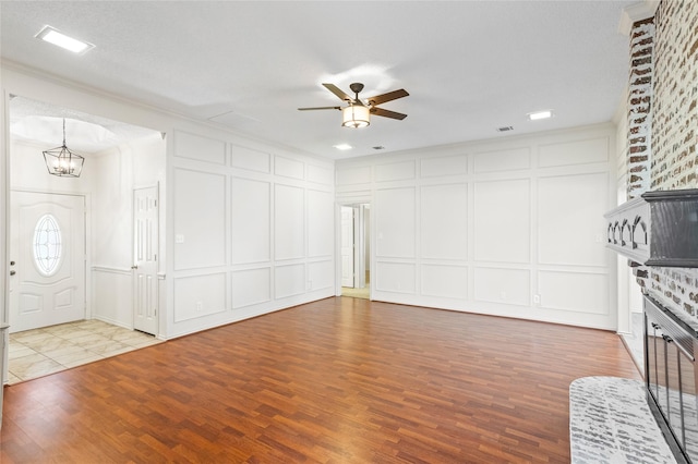 unfurnished living room with wood-type flooring, a brick fireplace, ornamental molding, and ceiling fan with notable chandelier