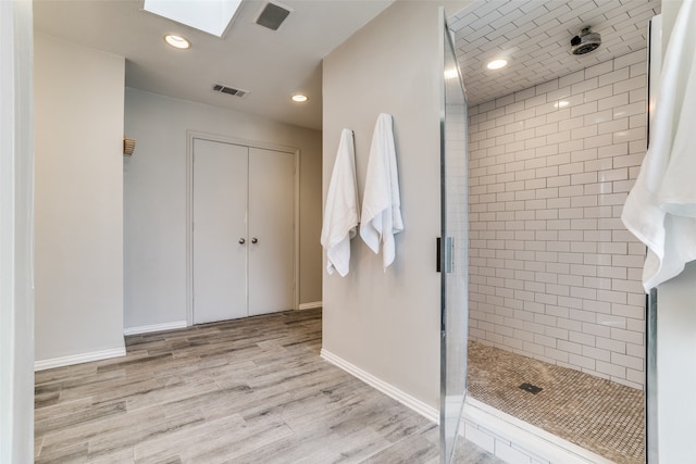 bathroom with hardwood / wood-style floors, tiled shower, and a skylight