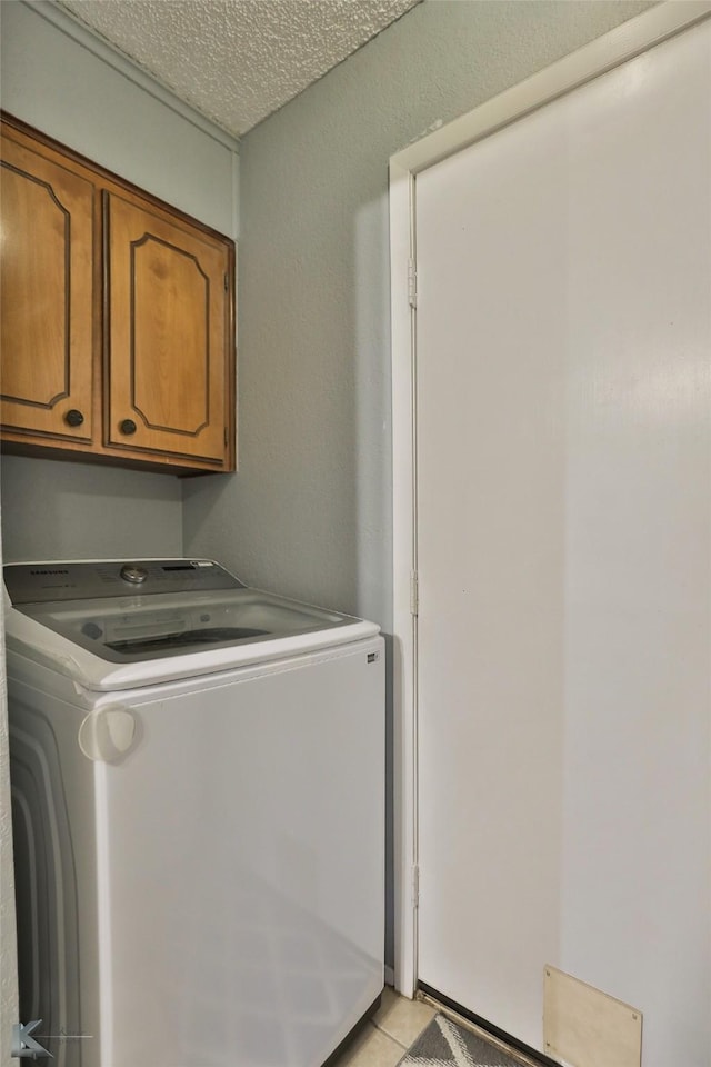 laundry area with light tile patterned floors, washer / dryer, cabinets, and a textured ceiling