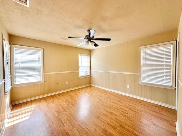 spare room with visible vents, wainscoting, ceiling fan, a textured ceiling, and light wood-type flooring