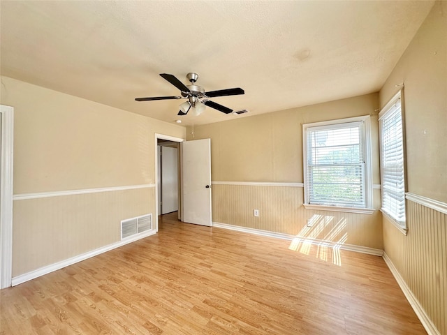 unfurnished room featuring a textured ceiling, wainscoting, visible vents, and light wood-style floors