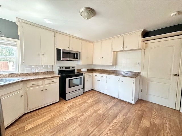 kitchen featuring stainless steel appliances, sink, tasteful backsplash, cream cabinetry, and light hardwood / wood-style flooring