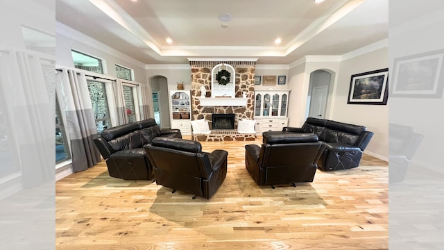 living room featuring crown molding, light hardwood / wood-style flooring, a tray ceiling, and a stone fireplace