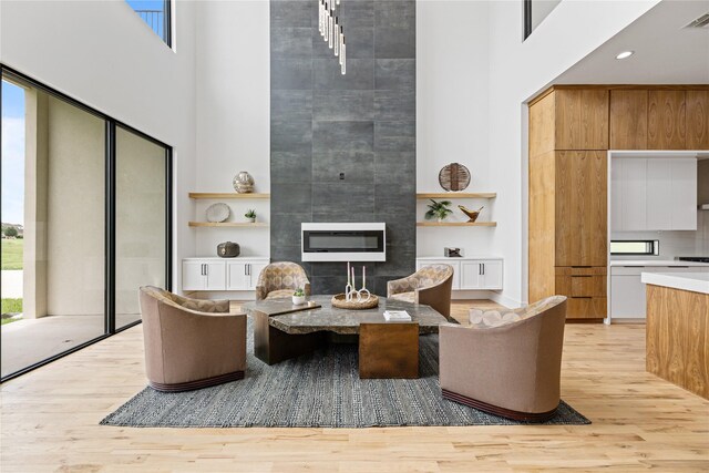 living room with a tile fireplace, a towering ceiling, and light hardwood / wood-style flooring