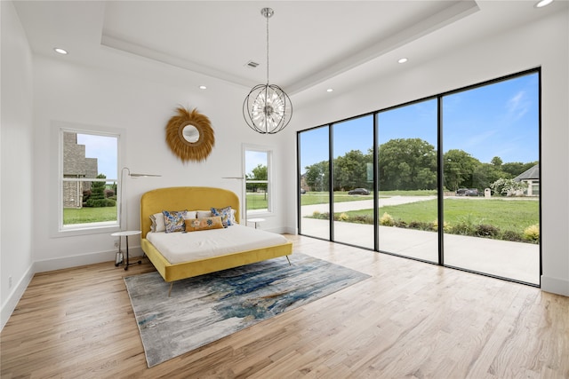 bedroom featuring a notable chandelier, access to exterior, a raised ceiling, and light hardwood / wood-style floors