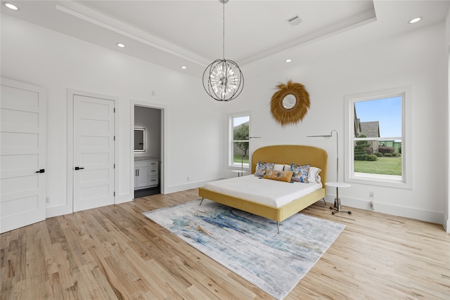 bedroom featuring connected bathroom, light hardwood / wood-style flooring, a raised ceiling, and a notable chandelier