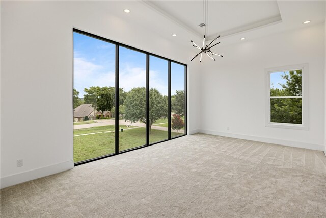 empty room featuring carpet flooring, a tray ceiling, a chandelier, and plenty of natural light