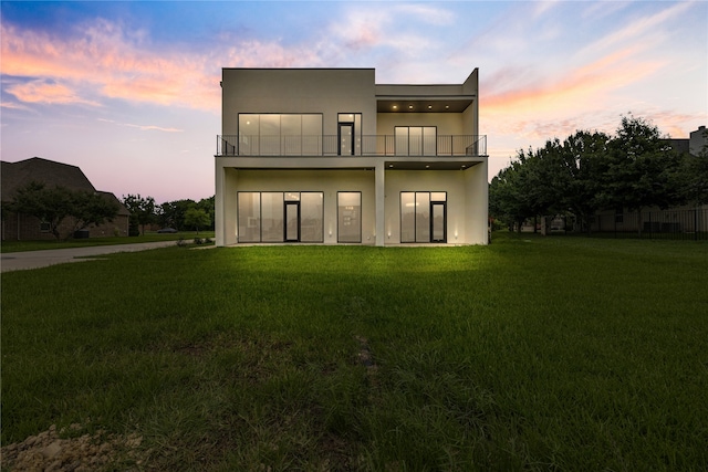 back house at dusk featuring a balcony and a yard