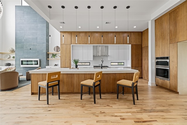 kitchen with hanging light fixtures, a breakfast bar, stainless steel double oven, sink, and light hardwood / wood-style flooring