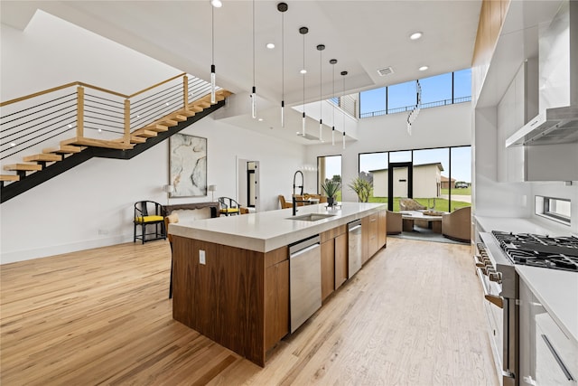 kitchen featuring hanging light fixtures, a kitchen island with sink, gas range, light hardwood / wood-style floors, and wall chimney exhaust hood