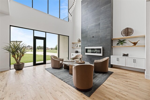 living room with a tile fireplace, light wood-type flooring, and a high ceiling